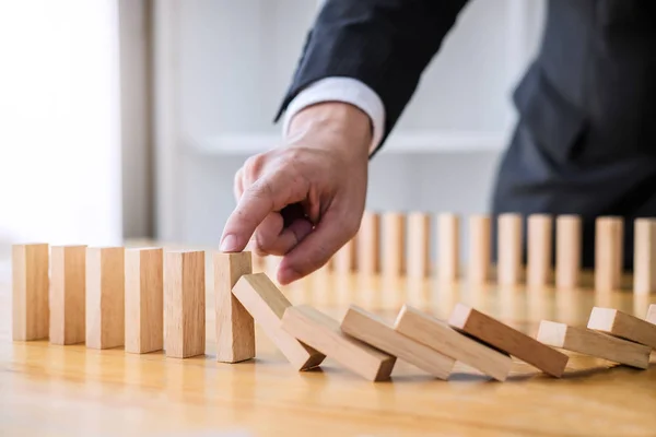 Wooden game strategy, Businessman hand stopping falling wooden dominoes effect from continuous toppled or risk, strategy and successful intervention concept for business.