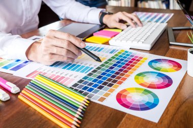 İş yerinde iş araçları ve aksesuarlarıyla renk seçimi ve grafik tableti üzerinde çalışan erkek yaratıcı grafik tasarımcı resmi.