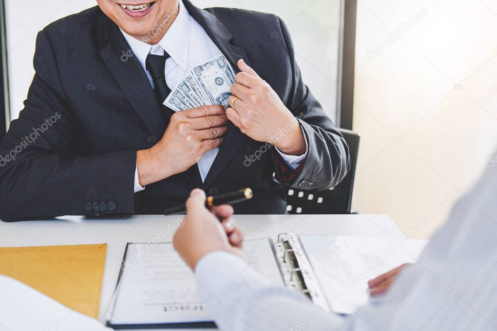 Bribery and corruption concept, bribe in the form of dollar bills, Businessman giving money while making deal to agreement a real estate contract and financial accounting.