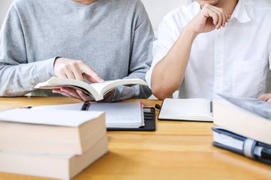 Eğitim, öğretim, öğrenme konsepti. Lise öğrencileri ya da sınıf arkadaşları kütüphanede ders çalışıp birlikte okuyorlar. Arkadaşların ödevlerini yapmasına ve giriş sınavına hazırlanmasına yardımcı oluyorlar..