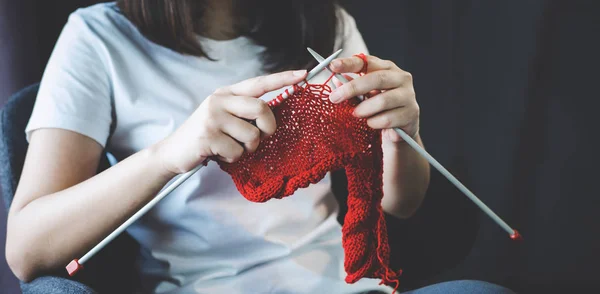 Close up shot of young woman hands knitting a red scarf handicraft in the living room on terrace at home.