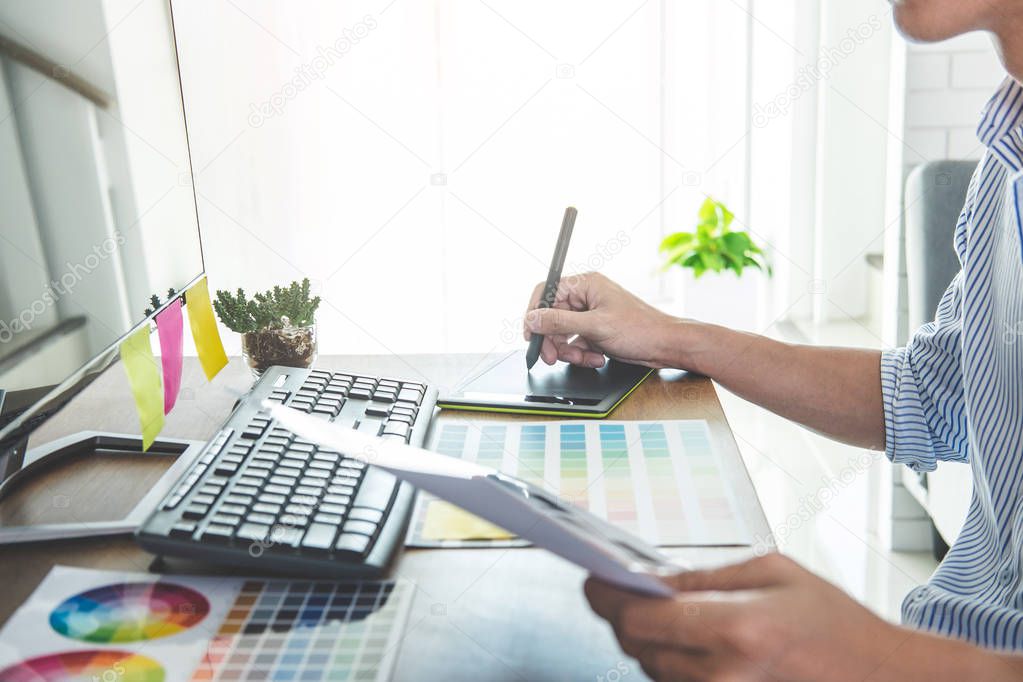 Image of male creative graphic designer working on color selection and drawing on graphics tablet at workplace with work tools and accessories in workspace.