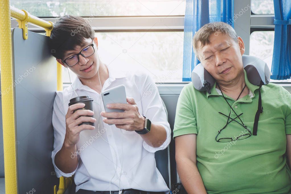 Young Asian man traveler sitting on a bus using smartphone for listening music and mature men sleeping with pillow, transport, tourism and road trip concept.