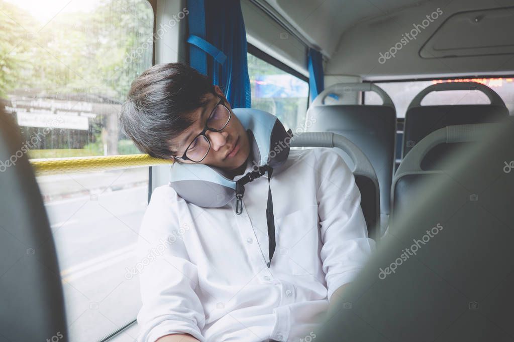 Young Asian man traveler sitting on a bus and sleeping with pillow, transport, tourism and road trip concept.