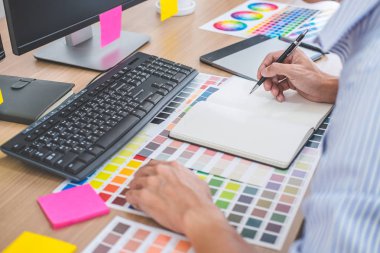 İş yerindeki iş araçları ve aksesuarlarla renk seçimi ve grafik tableti üzerinde çalışan erkek yaratıcı grafik tasarımcısının resmi.