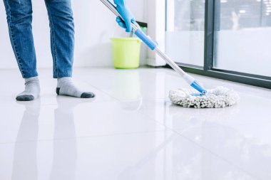 Oda temizliği ve temizlik konsepti mavi eldivenli mutlu genç kadın evde yerleri temizlerken paspas kullanıyor..