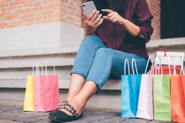 Tüketim, alışveriş, yaşam kavramı, smartphone alışveriş zevk oynarken alışveriş torbaları ve hediye kutusu yakın oturan genç kadın.
