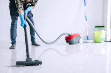 Temizlik ve ev işleri kavramı, bir elektrik süpürgesi katta evde kullanarak mavi kauçuk eldiven mutlu genç adam Temizleme.