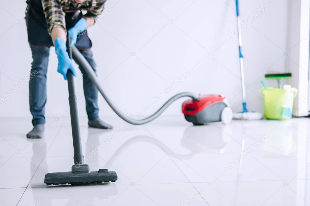 Housekeeping and housework cleaning concept, Happy young man in blue rubber gloves using a vacuum cleaner on floor at home.