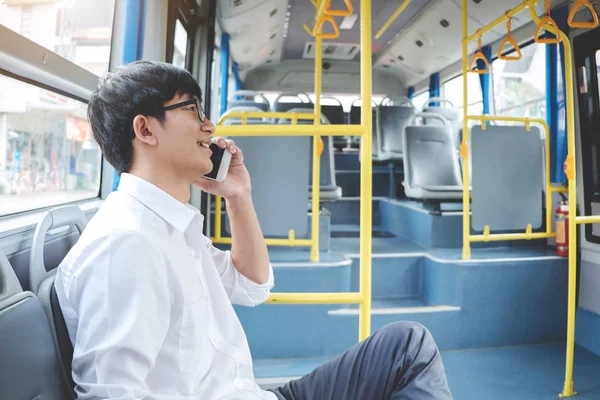 Young Asian man traveler sitting on a bus talking and using smartphone while smile of happy, transport, tourism and road trip concept.
