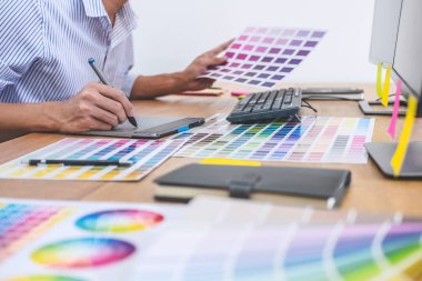 İş yerindeki iş araçları ve aksesuarlarla renk seçimi ve grafik tableti üzerinde çalışan erkek yaratıcı grafik tasarımcısının resmi.