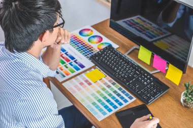 İş yerindeki iş araçları ve aksesuarlarla renk seçimi ve grafik tableti üzerinde çalışan erkek yaratıcı grafik tasarımcısının resmi.