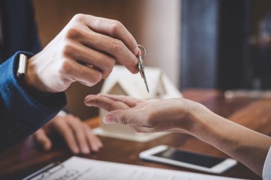 Emlakçı Satış Müdürü, kira kontratı ve konut sigortası için ipotek kredisi teklifiyle ilgili satış sözleşmesini imzaladıktan sonra müşterinin dosyalama anahtarlarını tutuyor..