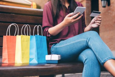 Tüketim, alışveriş, yaşam kavramı, smartphone tarafından zevk alışveriş alışveriş torbaları ve hediye kutusu ödeme sırasında yakın oturan genç kadın.