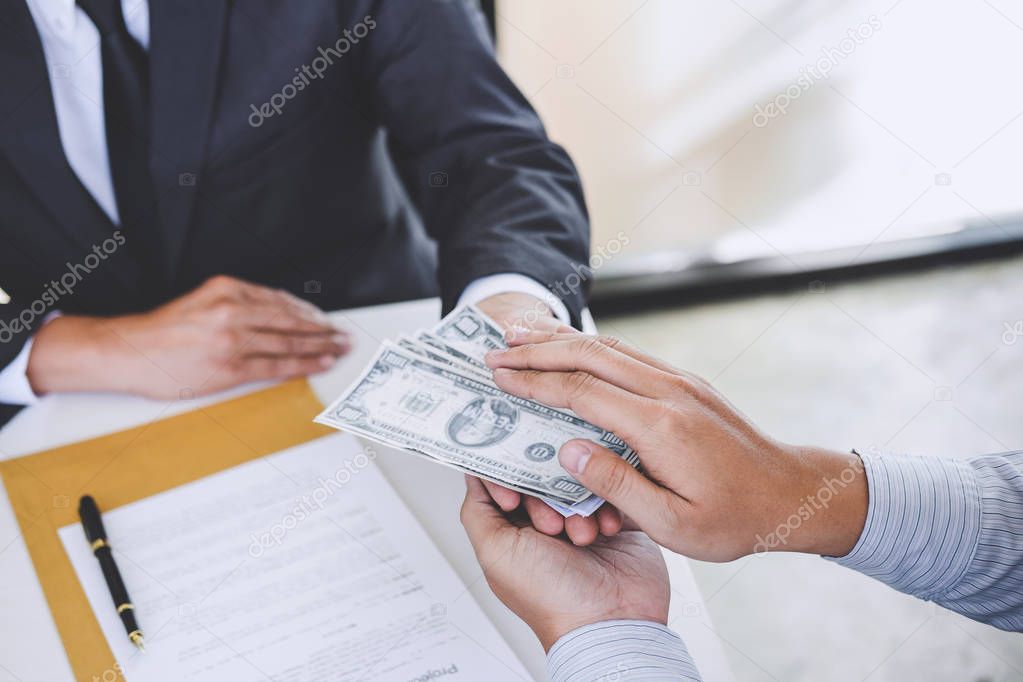 Bribery and corruption concept, bribe in the form of dollar bills, Businessman giving money while making deal to agreement a real estate contract.