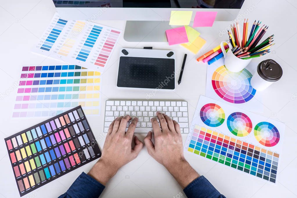 Image of male creative graphic designer working on color selection and drawing on graphics tablet at workplace with work tools and accessories, top view workspace.