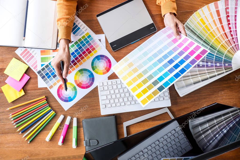 Image of female creative graphic designer working on color selection and drawing on graphics tablet at workplace with work tools and accessories, top view workspace.