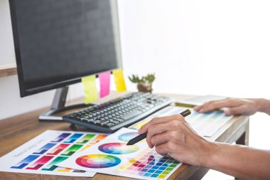 İş yerindeki iş araçları ve aksesuarlarla renk seçimi ve grafik tableti üzerinde çalışan erkek yaratıcı grafik tasarımcısının resmi.