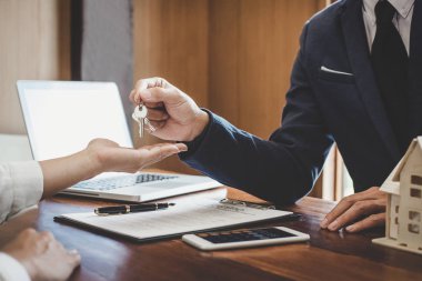 Emlakçı Satış Müdürü, kira kontratı ve konut sigortası için ipotek kredisi teklifiyle ilgili satış sözleşmesini imzaladıktan sonra müşterinin dosyalama anahtarlarını tutuyor..