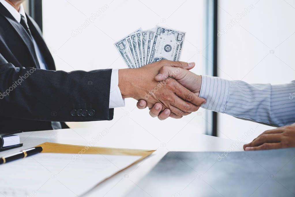 Bribery and corruption concept, bribe in the form of dollar bills, Businessman shaking hands and giving hides money while making deal to agreement a contract.