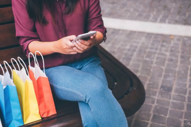 Tüketim, alışveriş, yaşam kavramı, smartphone alışveriş zevk oynarken alışveriş torbaları ve hediye kutusu yakın oturan genç kadın.