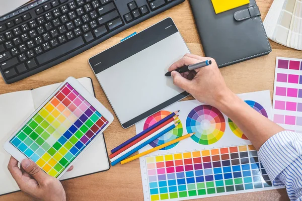 Image of male creative graphic designer working on color selection and drawing on graphics tablet at workplace with work tools and accessories in workspace.