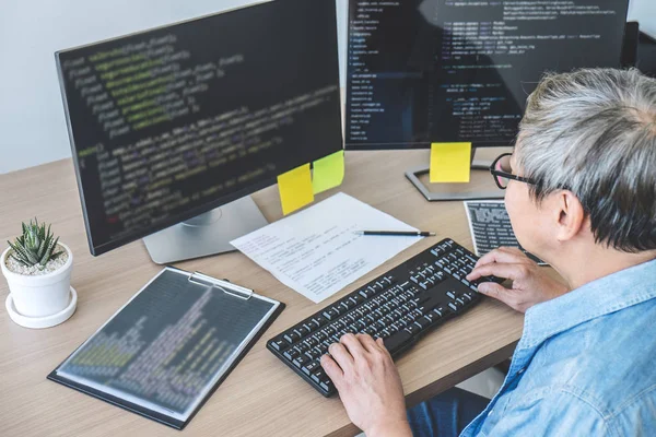 Senior Professional programmer working at developing programming and website working in a software develop company office, writing codes and typing data code.