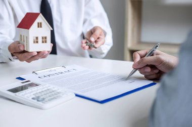 Emlakçı Satış Müdürü, kira kontratı ve konut sigortası için ipotek kredisi teklifiyle ilgili satış sözleşmesini imzaladıktan sonra müşterinin dosyalama anahtarlarını tutuyor..
