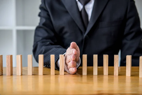 Wooden game strategy, Businessman hand stopping falling wooden dominoes effect from continuous toppled or risk, strategy and successful intervention concept for business.