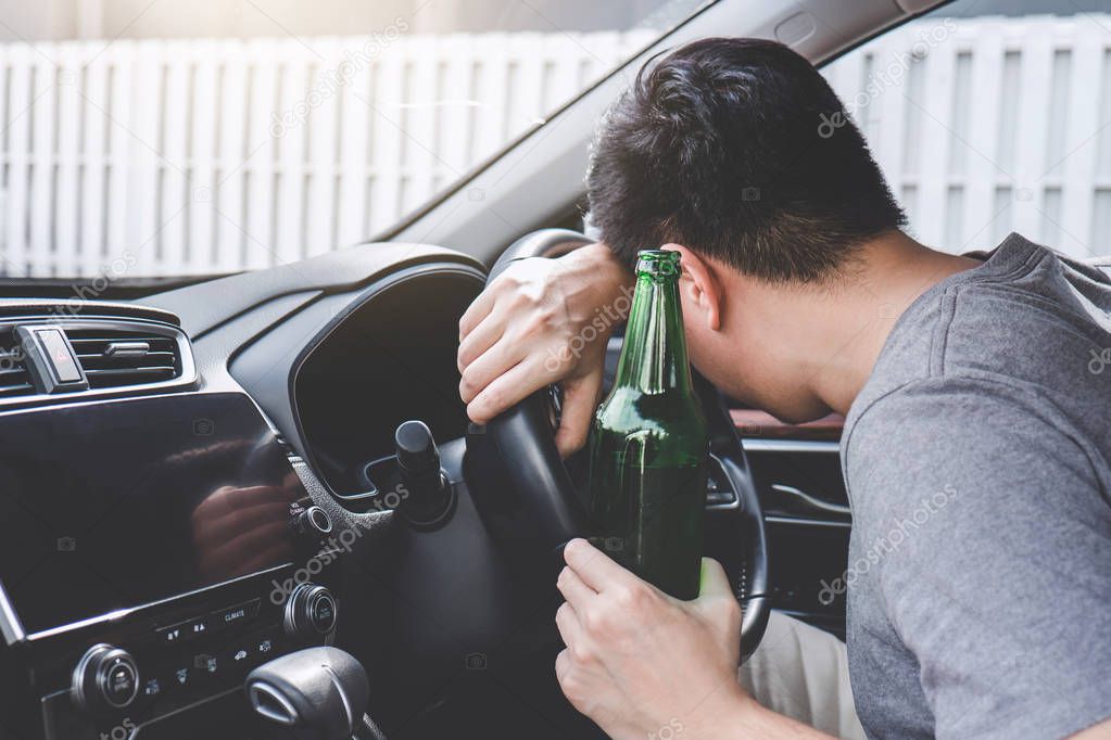 Young asian man drives a car with drunk a bottle of beer and fall asleep behind the wheel of a car.