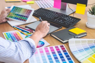 İş yerindeki iş araçları ve aksesuarlarla renk seçimi ve grafik tableti üzerinde çalışan erkek yaratıcı grafik tasarımcısının resmi.