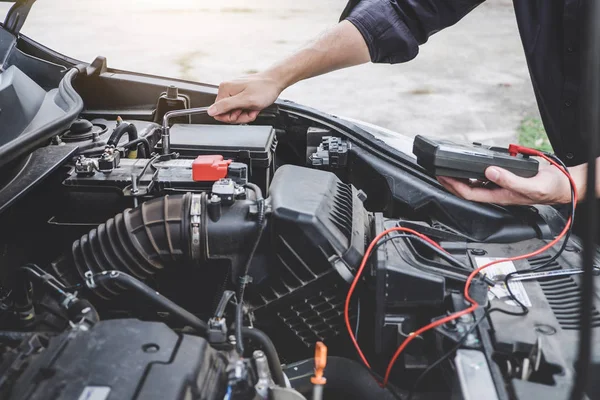 Services car engine machine concept, Automobile mechanic repairman hands repairing a car engine automotive workshop with a wrench and digital multimeter testing battery, car service and maintenance.