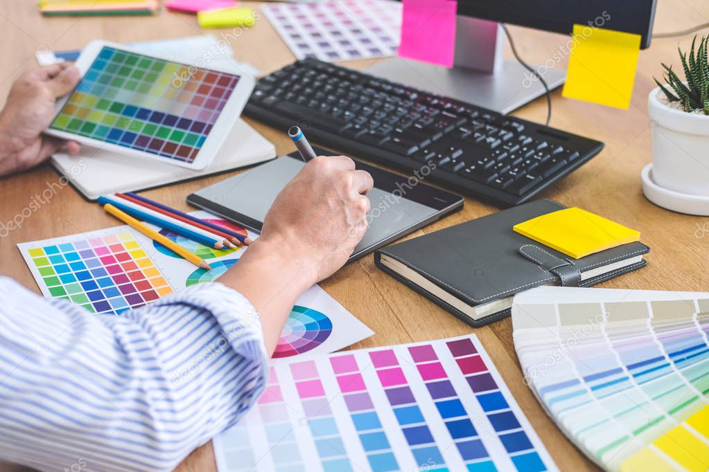 Image of male creative graphic designer working on color selection and drawing on graphics tablet at workplace with work tools and accessories in workspace.