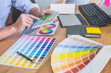 İş yerindeki iş araçları ve aksesuarlarla renk seçimi ve grafik tableti üzerinde çalışan erkek yaratıcı grafik tasarımcısının resmi.