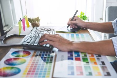 İş yerindeki iş araçları ve aksesuarlarla renk seçimi ve grafik tableti üzerinde çalışan erkek yaratıcı grafik tasarımcısının resmi.