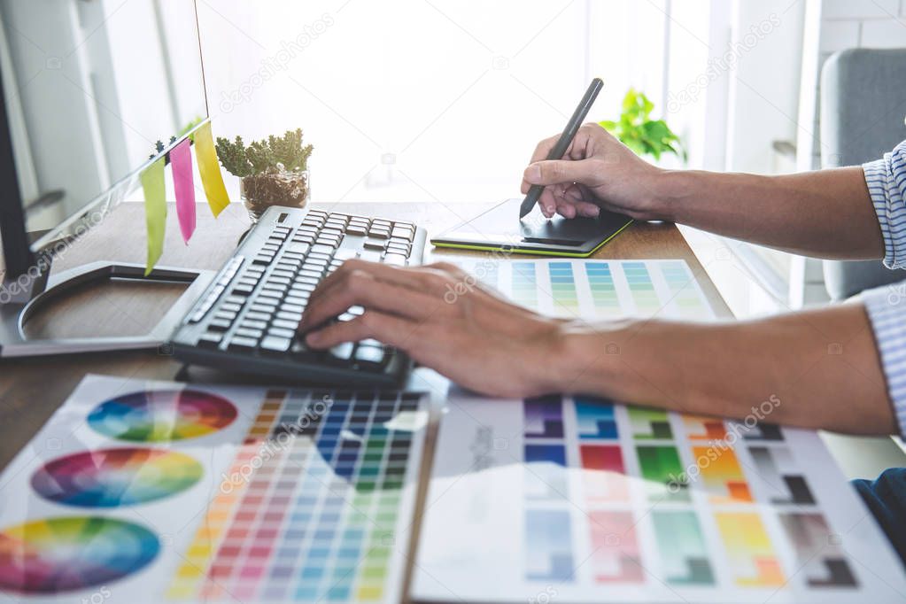 Image of male creative graphic designer working on color selection and drawing on graphics tablet at workplace with work tools and accessories in workspace.