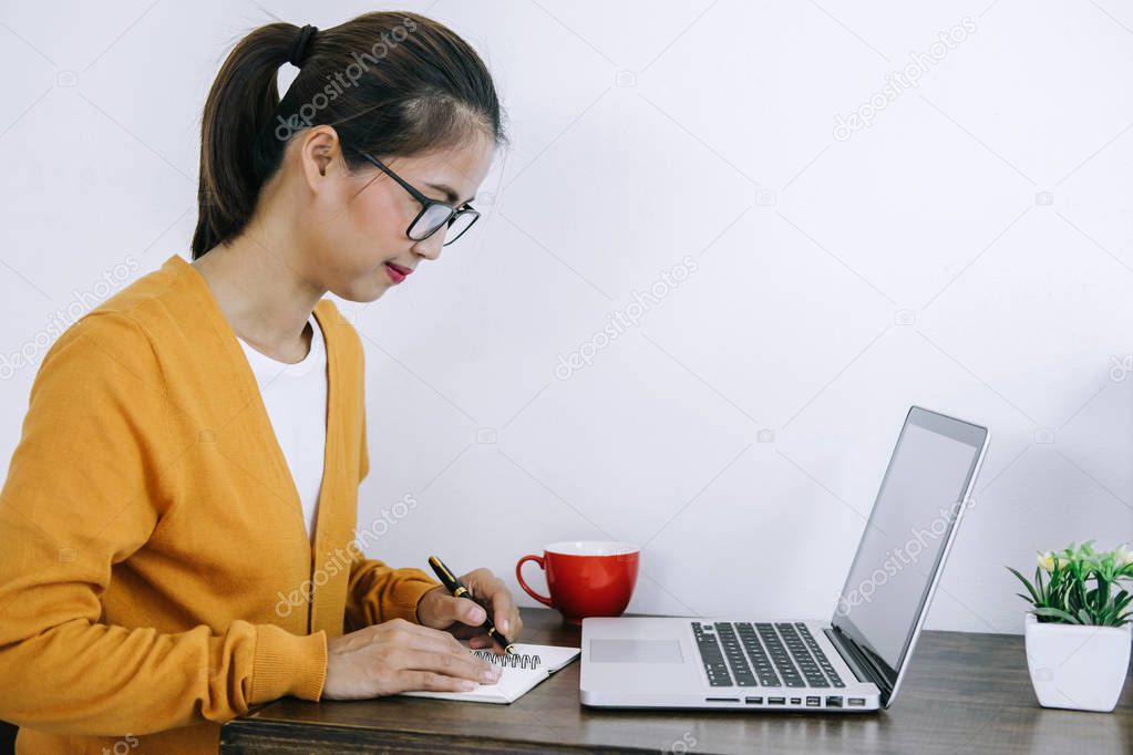 Happy casual young asian woman working in home or small office with using a laptop and document report on desk as a freelancer.