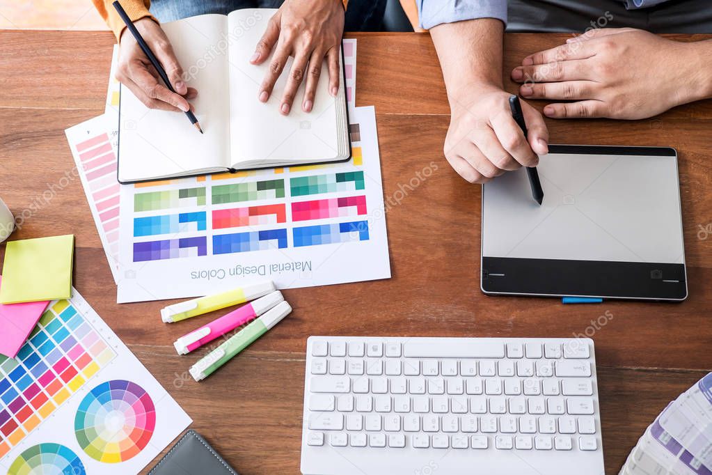 Two colleague creative graphic designer working on color selection and color swatches, drawing on graphics tablet at workplace with work tools and accessories, top view space.