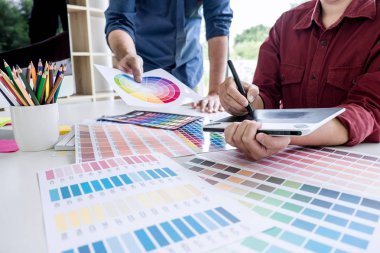 Renk seçimi ve renk örnekleri üzerinde çalışan iki iş arkadaşı yaratıcı grafik tasarımcısı, çalışma araçları ve aksesuarlarla iş yerindeki grafik tabletine çizim yapıyor.