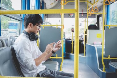 Küçük Asya adam video izle smartphone kullanarak veya gülümseme mutlu, ulaşım, turizm ve road trip kavramı ile müzik dinleme giden bir otobüse oturan gezgin.