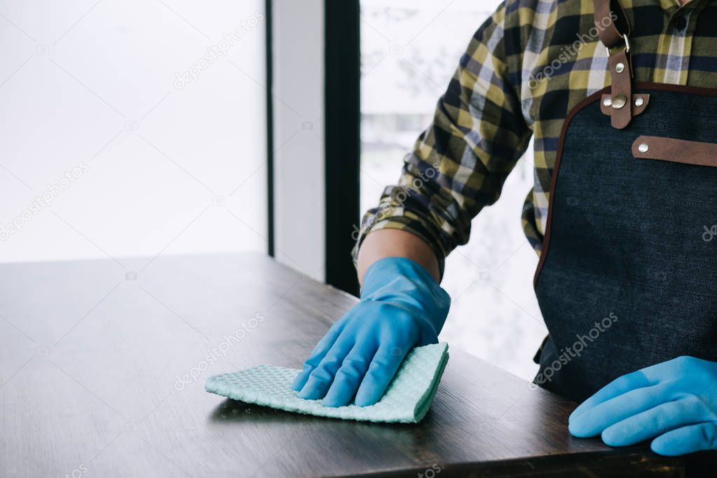 Husband housekeeping and cleaning concept, Happy young man wiping dust using a spray and a duster while cleaning on table at home.