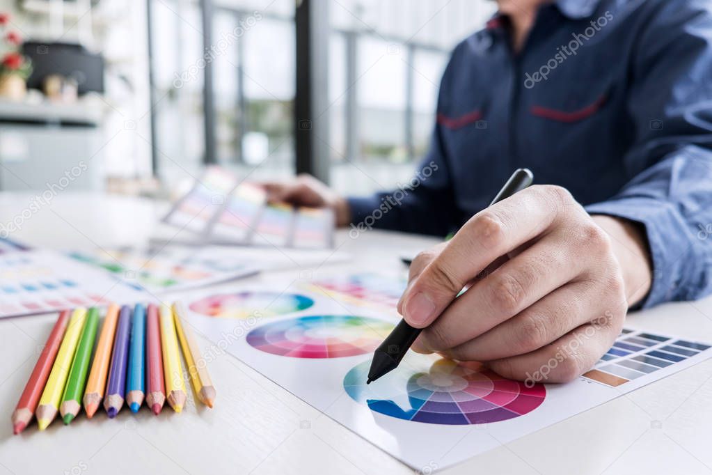 Image of male creative graphic designer working on color selection and drawing on graphics tablet at workplace with work tools and accessories.