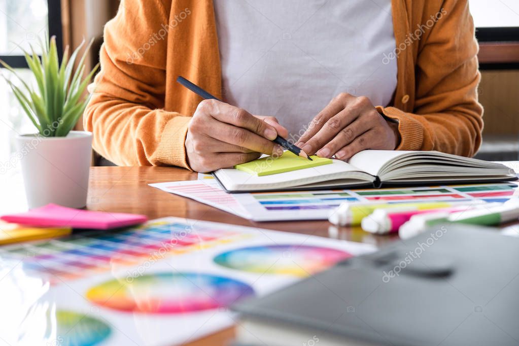 Image of female creative graphic designer working on color selection and drawing on graphics tablet at workplace with work tools and accessories.