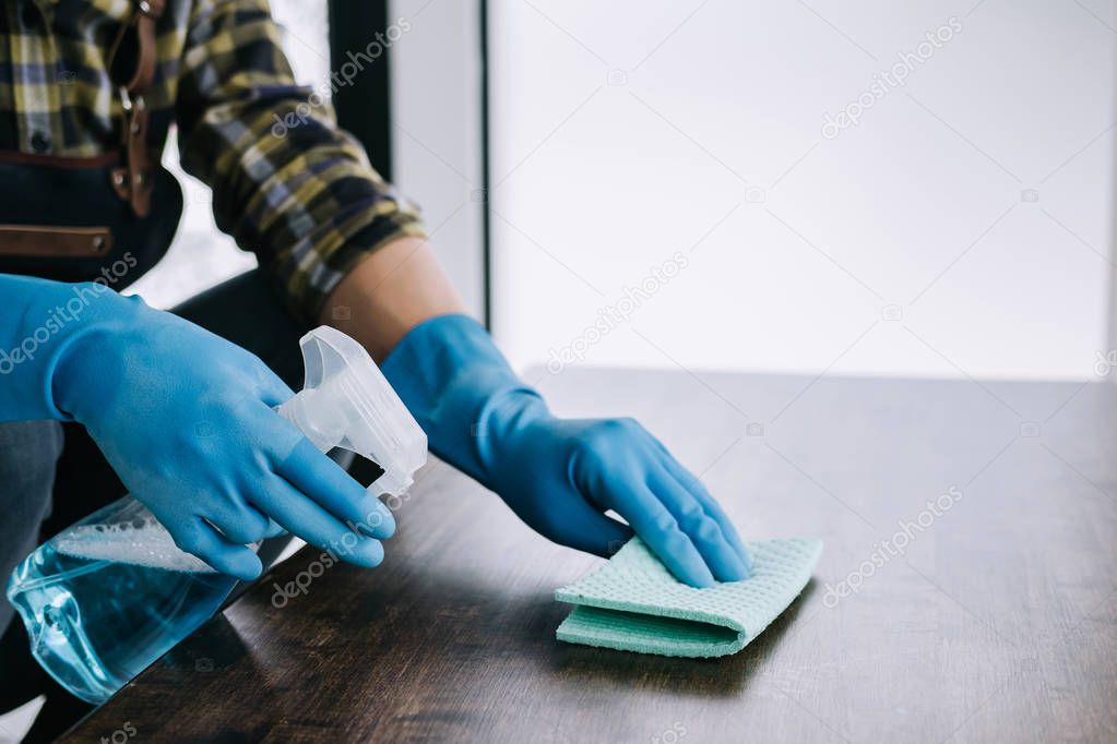 Husband housekeeping and cleaning concept, Happy young man wiping dust using a spray and a duster while cleaning on table at home.