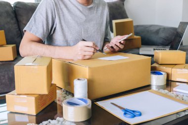 Genç girişimci KOBİ serbest adam smartphone kullanarak sipariş istemci almak ve satınalma siparişine ambalaj sıralama kutusu teslim online pazar ile çalışma ve paket ürün hazırlama.