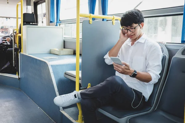 Young Asian man traveler sitting on a bus listening to music on smartphone while smile of happy, transport, tourism and road trip concept.