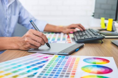 İş yerindeki iş araçları ve aksesuarlarla renk seçimi ve grafik tableti üzerinde çalışan erkek yaratıcı grafik tasarımcısının resmi.