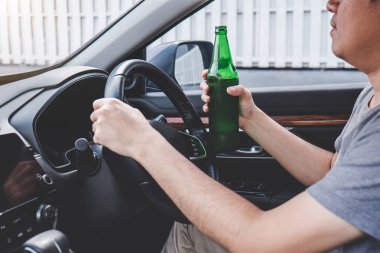 Genç Asyalı adam alkollü araba kullanıyor. Direksiyonda bir şişe bira var..