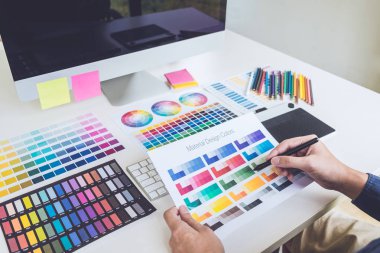 İş yerinde iş araçları ve aksesuarlarıyla renk seçimi ve grafik tableti üzerinde çalışan erkek yaratıcı grafik tasarımcı resmi.