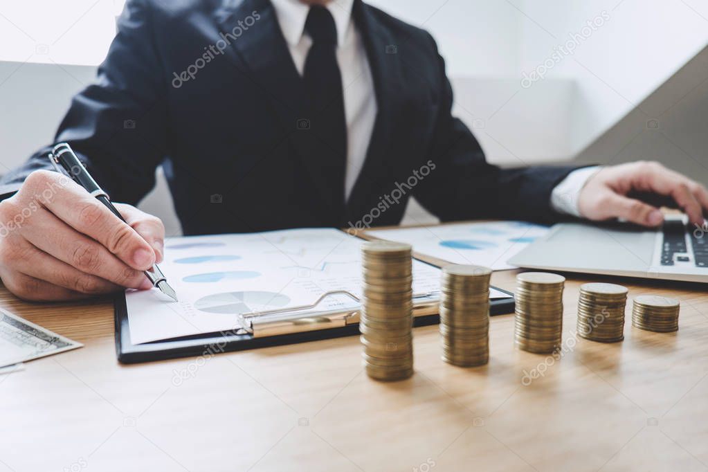 Businessman writing making report with stacked coins arranged at